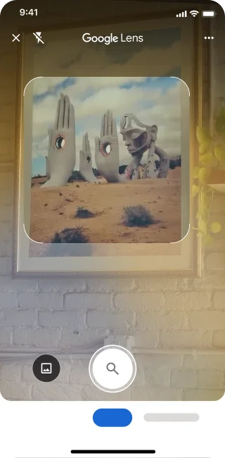 फ़ोन पर Google Lens ऐप्लिकेशन खुला है. सूचना से पता चलता है कि उपयोगकर्ता, शटर बटन पर टैप करके रेगिस्तान में मौजूद पत्थर से बनी बड़ी-बड़ी हाथ की मूर्तियों की इमेज खोज सकता है.